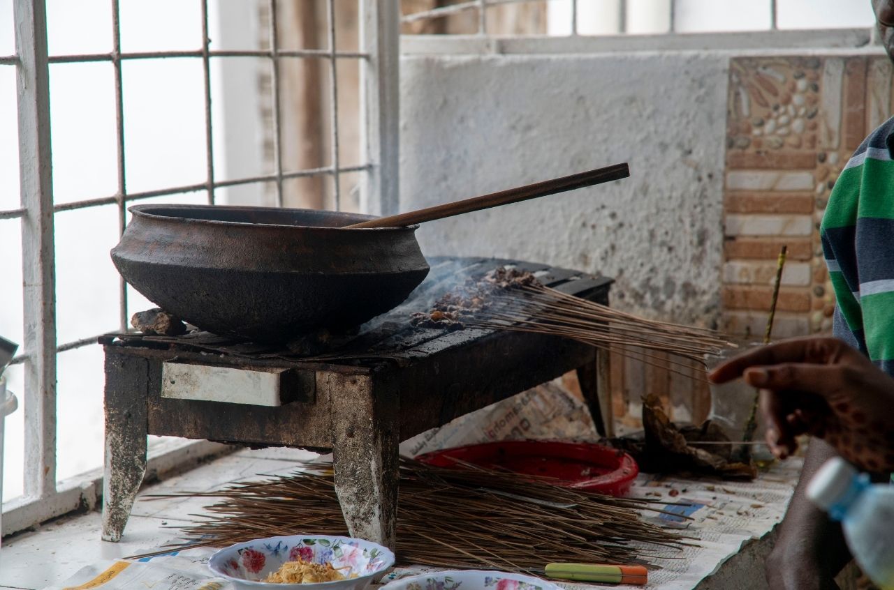 Street food vendor grilling meat skewers beside a pot in Zanzibar, Tanzania